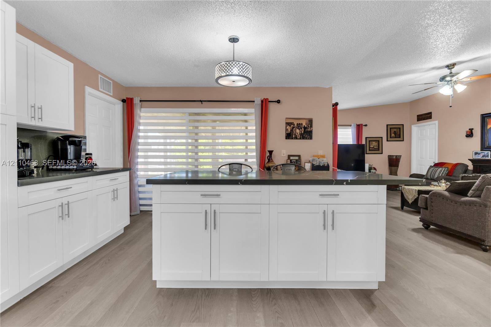 Kitchen featuring white shaker-style cabinetry, a central island with dark stone countertops, wood-finish flooring, and a contemporary drum pendant light fixture Kitchen featuring white shaker-style cabinetry, a central island with dark stone countertops, wood-finish flooring, and a contemporary drum pendant light fixture