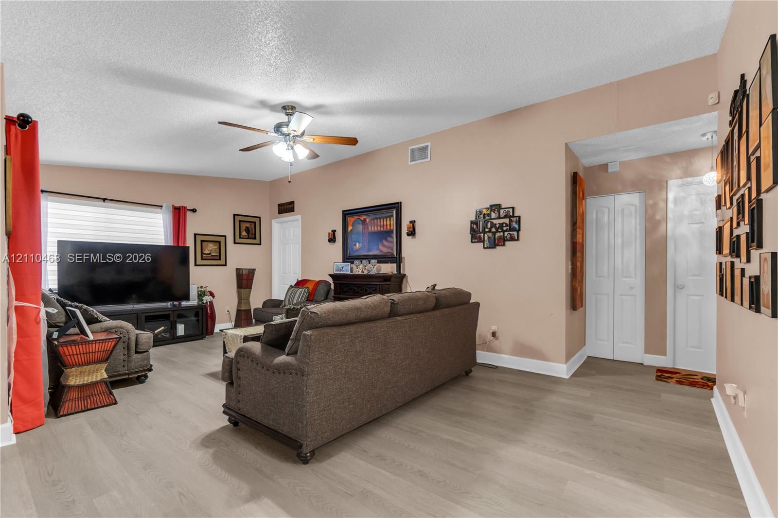 Living area featuring wood-finish flooring, a ceiling fan with integrated lighting, and white six-panel closet doors Living area featuring wood-finish flooring, a ceiling fan with integrated lighting, and white six-panel closet doors