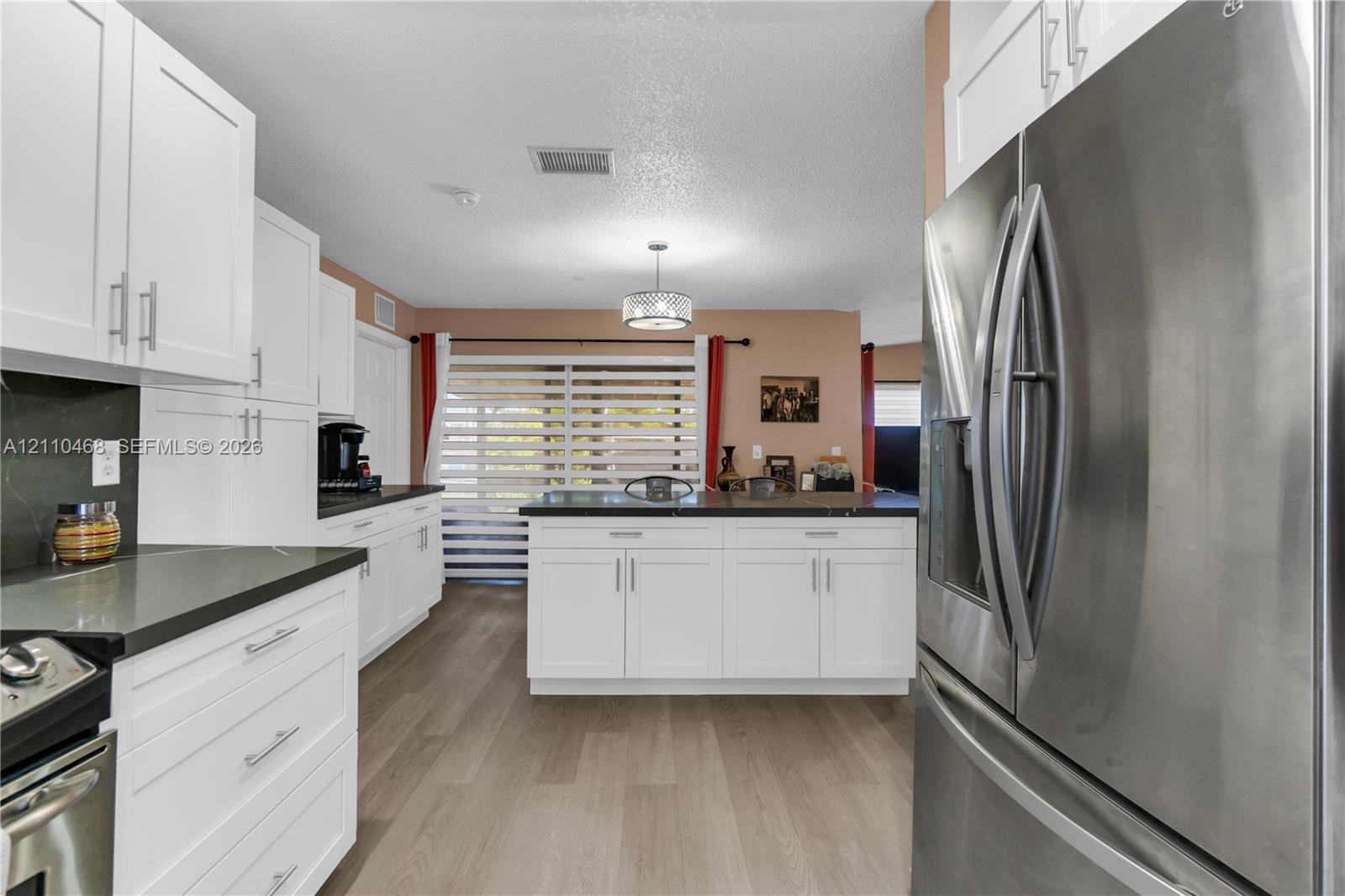 Kitchen featuring white shaker-style cabinetry, dark stone-finish countertops, stainless steel appliances, wood-finish flooring, and a central island