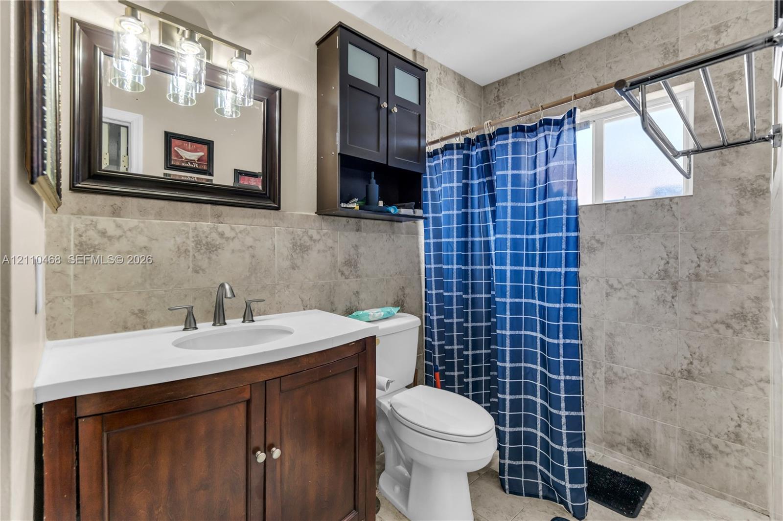 Bathroom featuring a wood-finish vanity with a white countertop, wall-mounted cabinetry, tile wall surfacing, and a three-light vanity fixture