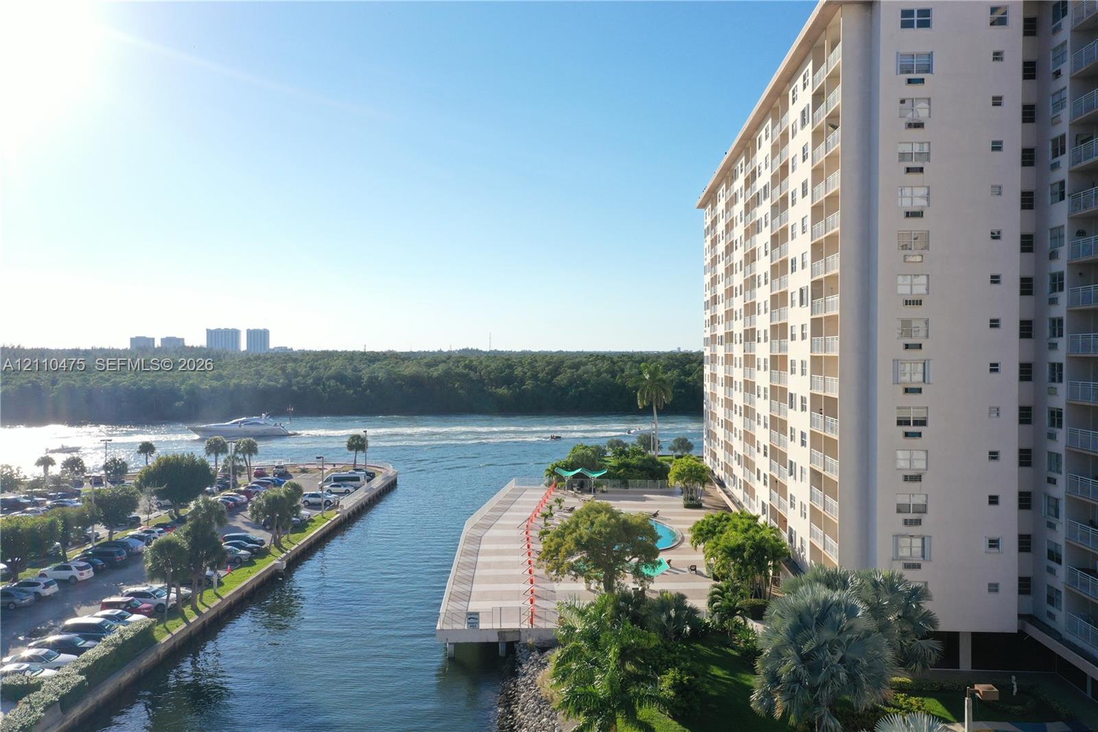 High-rise building exterior with a waterfront pool deck, paved hardscaping, mature palm trees, and canal-front positioning