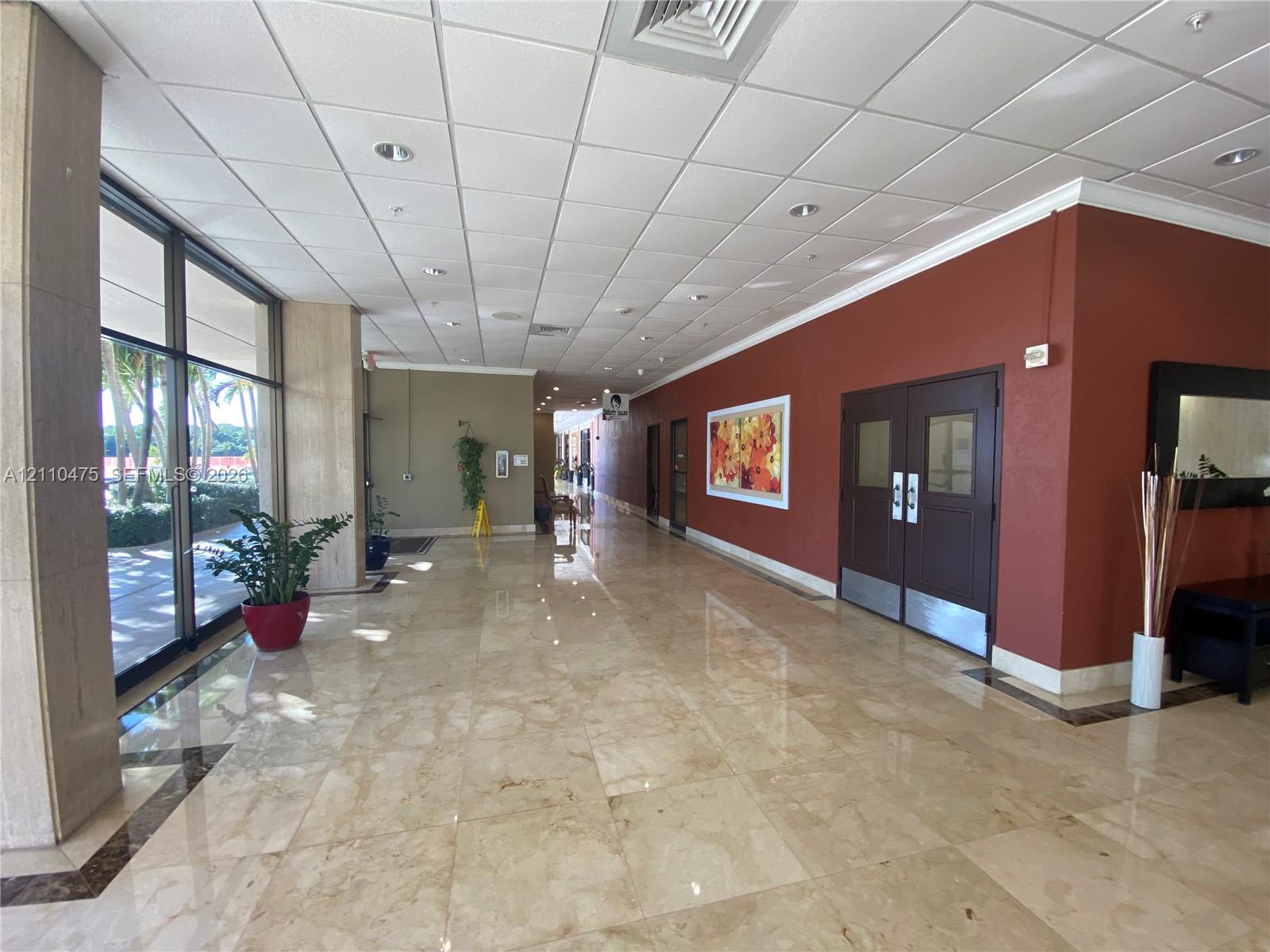 Spacious lobby featuring polished stone flooring, floor-to-ceiling glass windows, recessed ceiling lighting, and double-entry doors with metallic kick plates