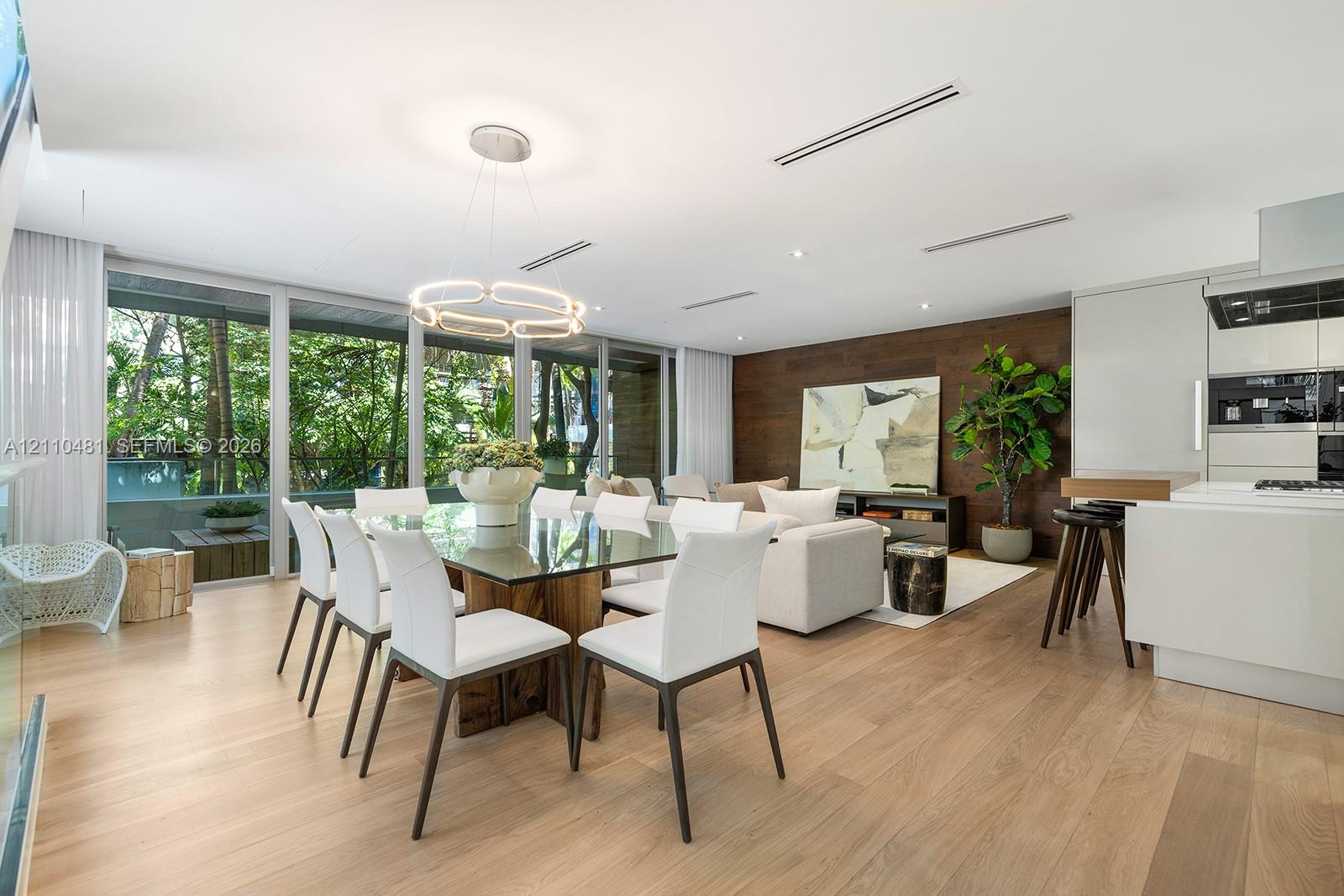 Open-concept living space featuring wood-finish flooring, floor-to-ceiling windows, a wood-paneled accent wall, and recessed linear lighting