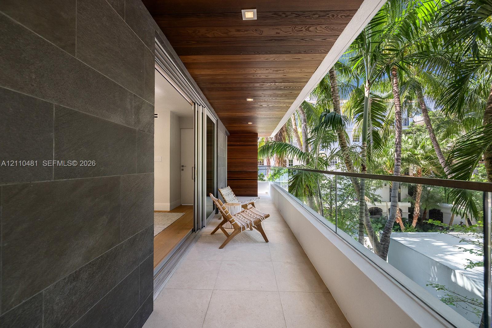 Covered balcony featuring large-format stone tile flooring, charcoal-toned stone wall cladding, natural wood-finish ceiling, and a glass panel railing