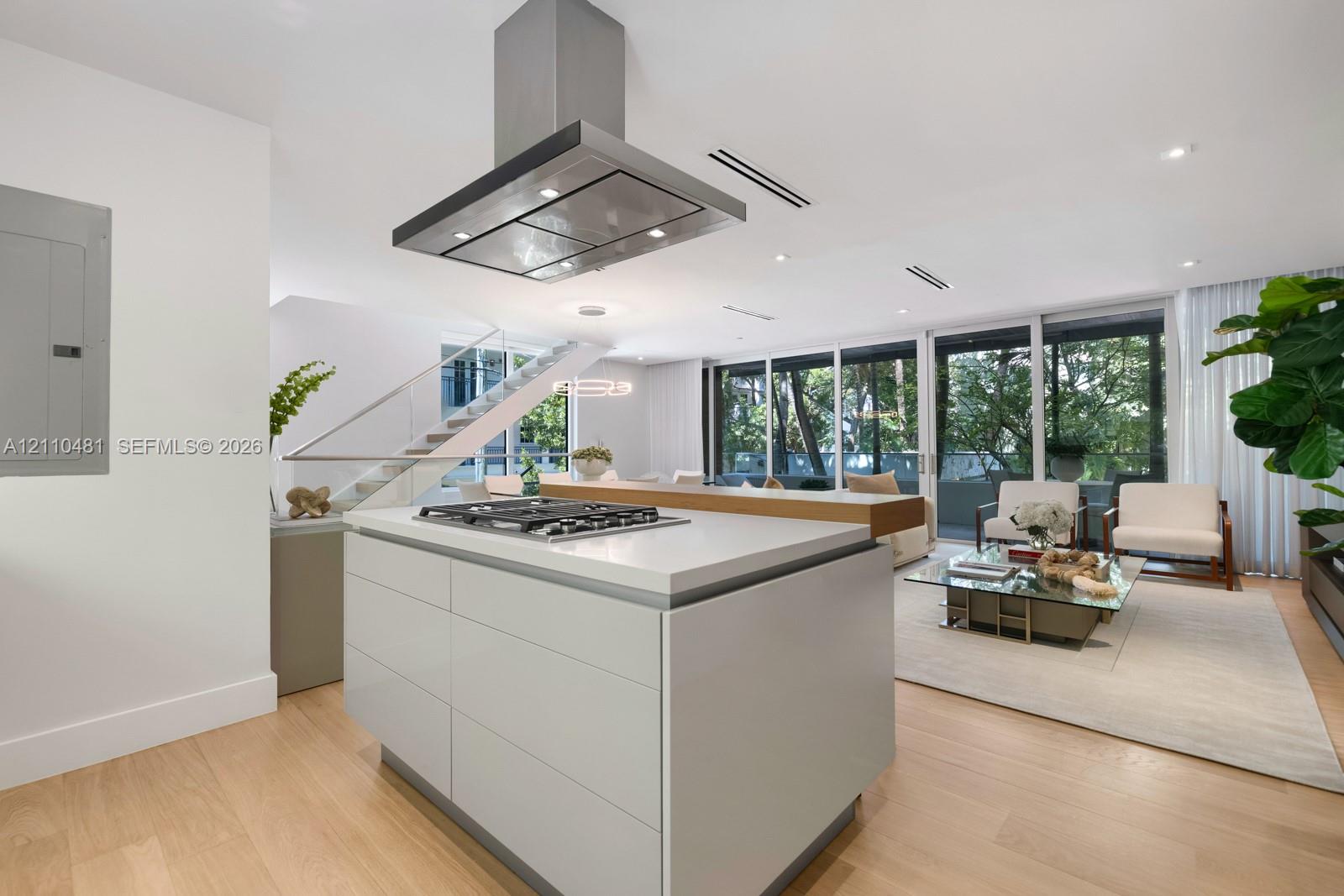 Kitchen island featuring a stone countertop, inset gas cooktop, and stainless steel hood range, complemented by wood-finish flooring and floor-to-ceiling windows