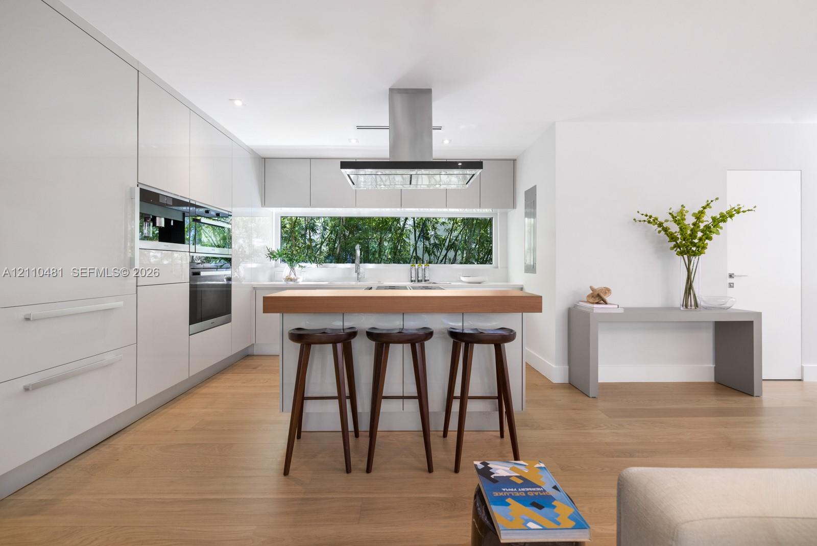 Contemporary kitchen featuring flat-panel cabinetry, stainless steel built-in ovens, wood-finish flooring, a center island with a wood countertop, and a stainless steel range hood