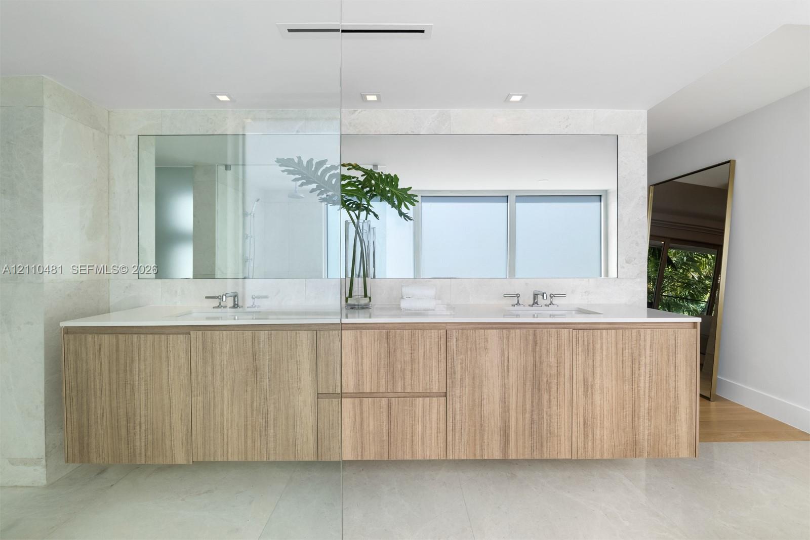 Floating vanity with wood-finish cabinetry, dual undermount sinks, quartz countertop, polished metal fixtures, and full-width wall mirror