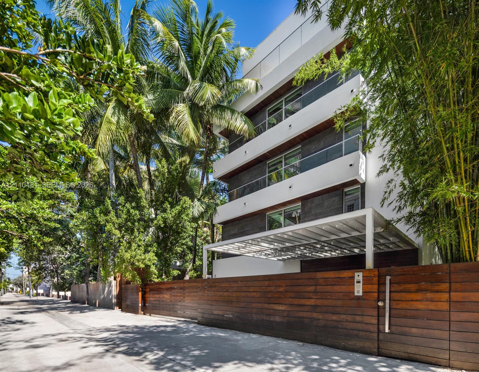 Multi-story contemporary exterior featuring horizontal wood siding, smooth white stucco facade, glass balcony railings, and a gated entrance with horizontal wood fencing