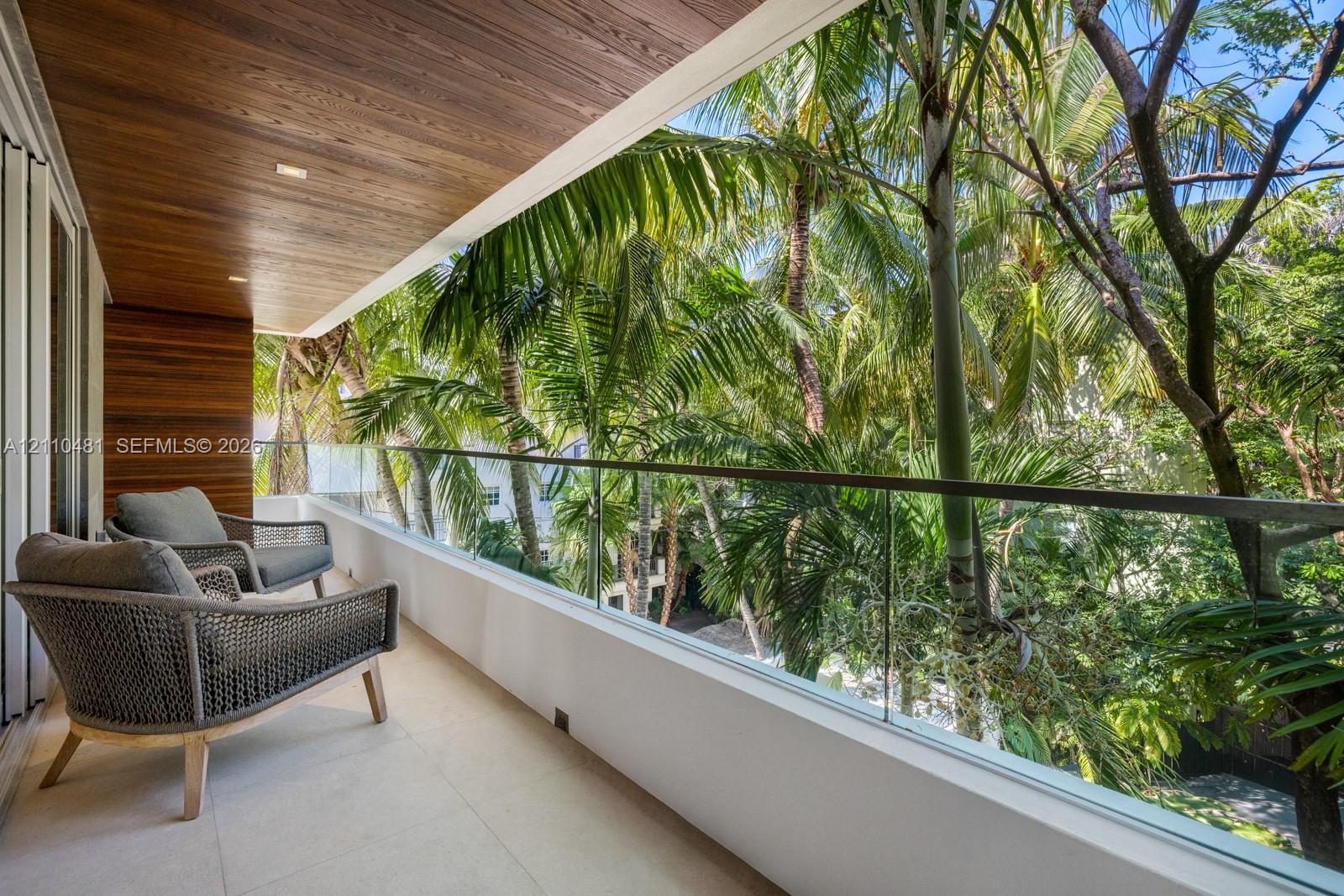 Covered balcony featuring wood-plank ceiling paneling, frameless glass railing, and light-toned tile flooring