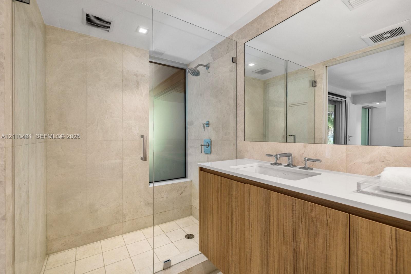Bathroom featuring stone-tile wall finishes, a wood-finish vanity with a white countertop, a frameless glass-enclosed shower, and a large wall-mounted mirror