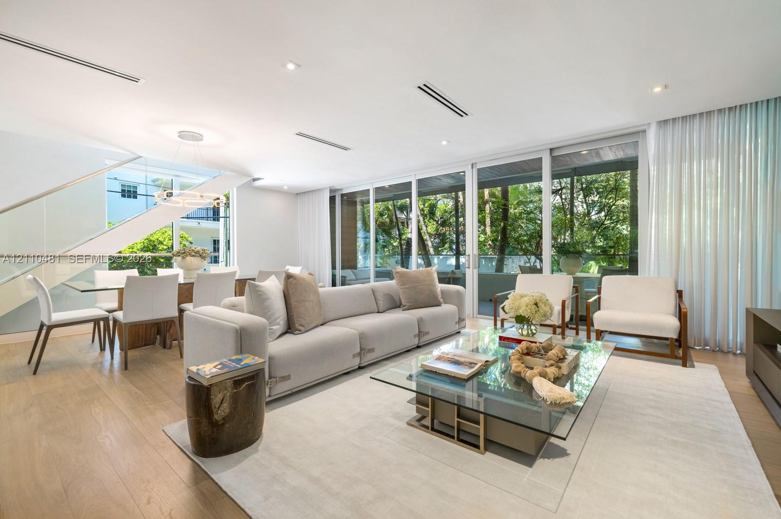 Open-concept living space featuring wood-finish flooring, floor-to-ceiling glass sliding doors, recessed ceiling lighting, and a floating staircase with a glass railing