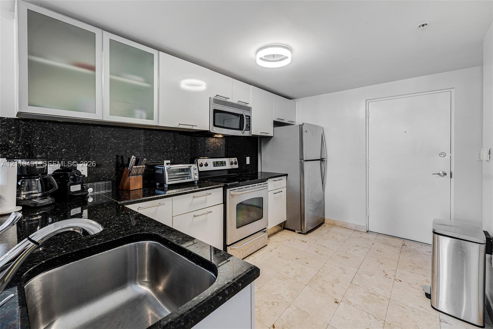 Kitchen featuring white cabinetry with glass-panel upper doors, dark stone countertops, stainless steel appliances, and tile flooring