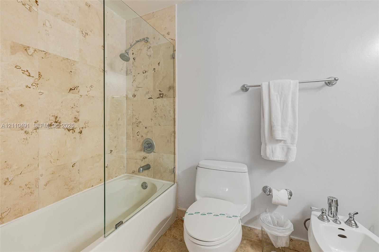 Bathroom featuring stone-tile wall surround, glass shower panel, soaking tub, chrome fixtures, and a white porcelain toilet and bidet
