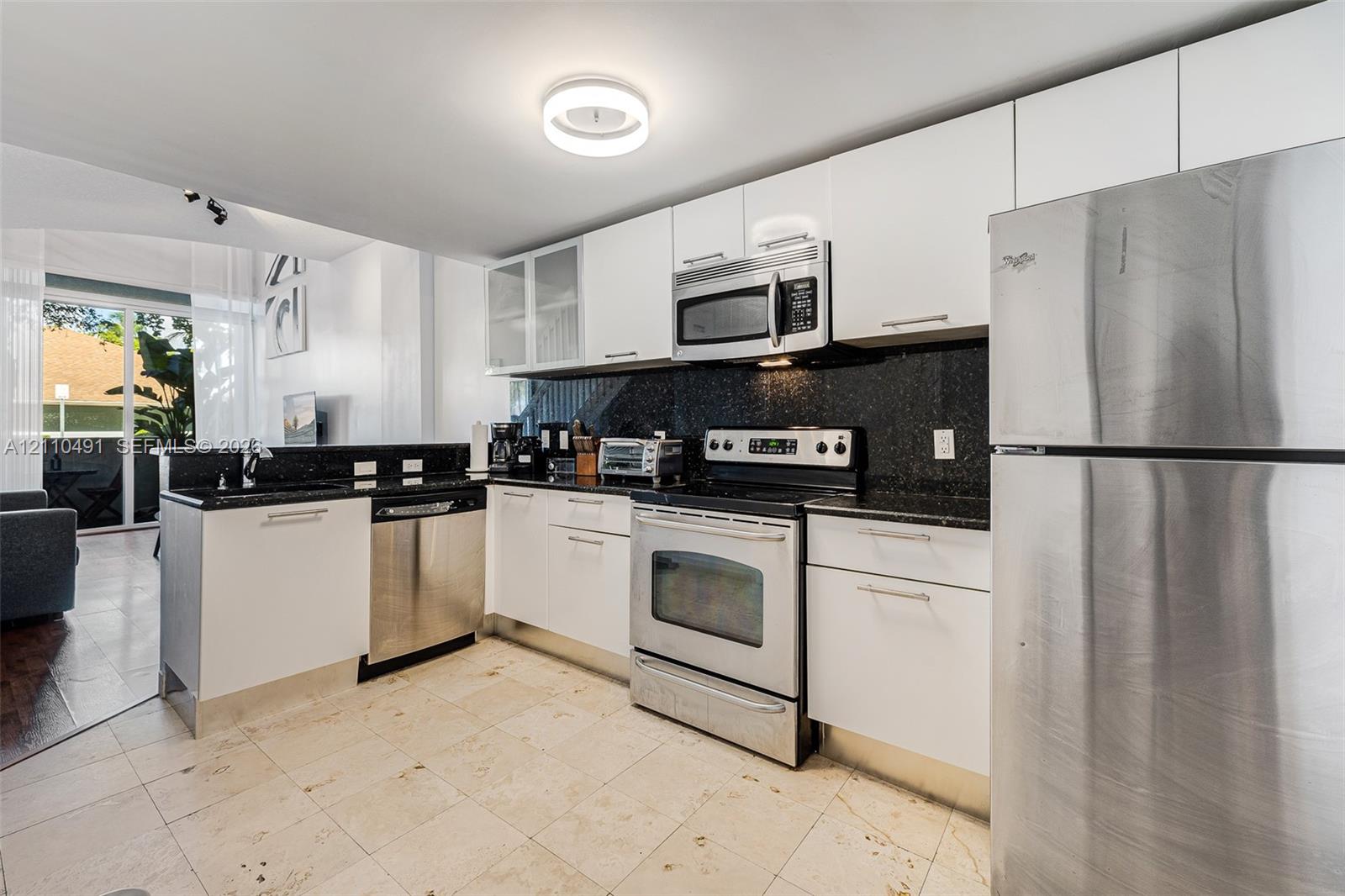 Kitchen featuring flat-panel white cabinetry, stone-finish countertops, stainless steel appliances, and tile flooring