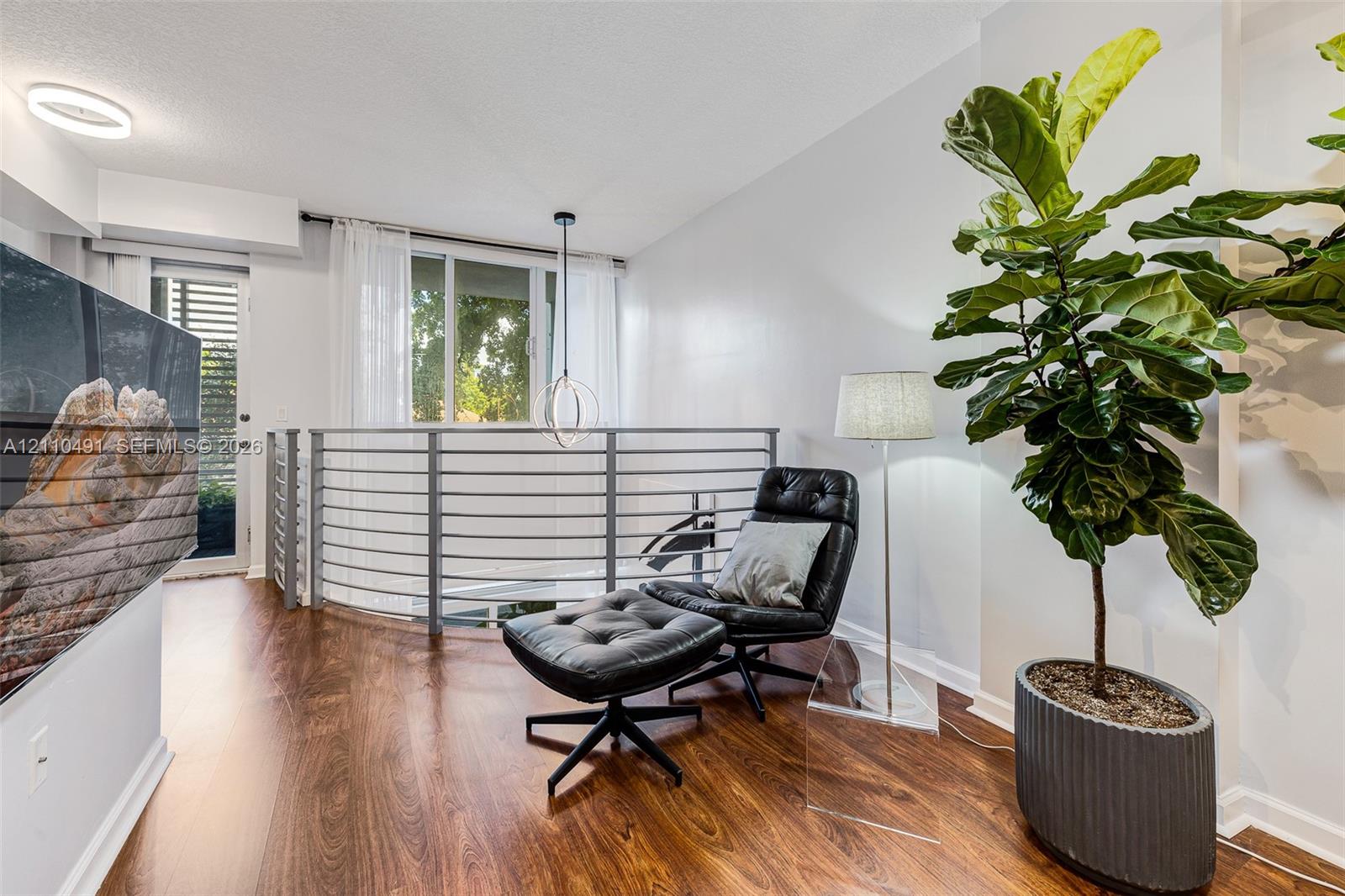 Open-concept loft area featuring wood-finish flooring, a contemporary circular pendant light, integrated horizontal metal railing, and recessed ceiling lighting