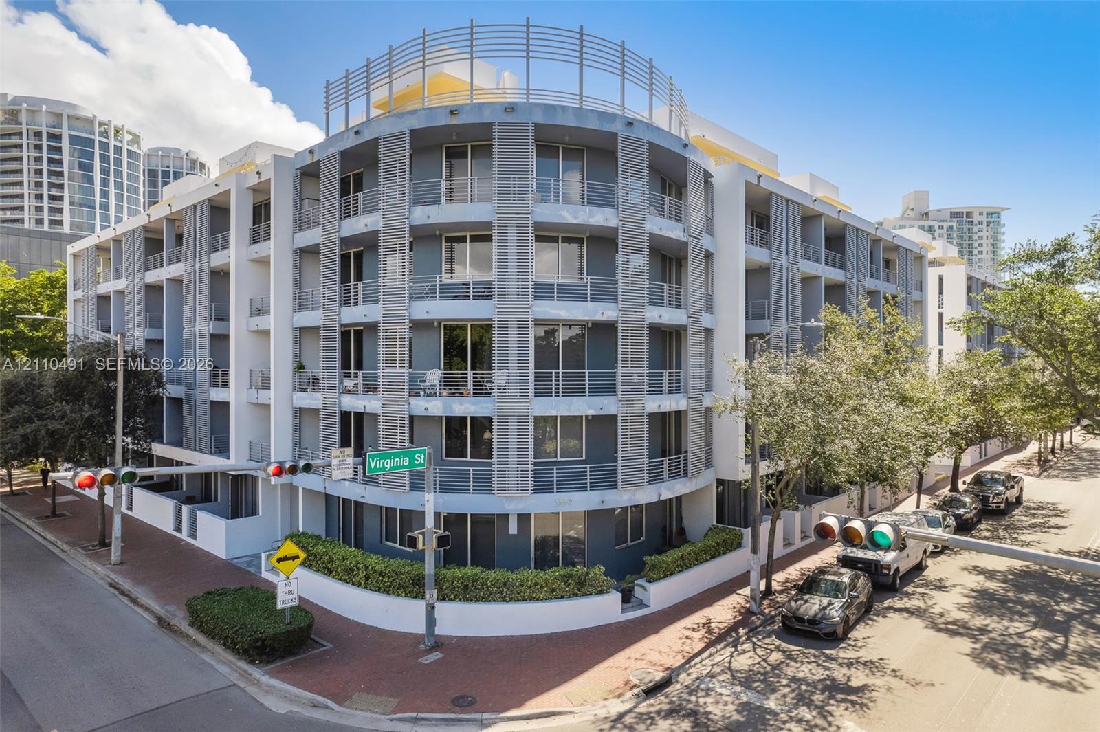 Multi-story contemporary exterior featuring curved architectural design, private recessed balconies, metallic louvered screening, and ground-level perimeter landscaping
