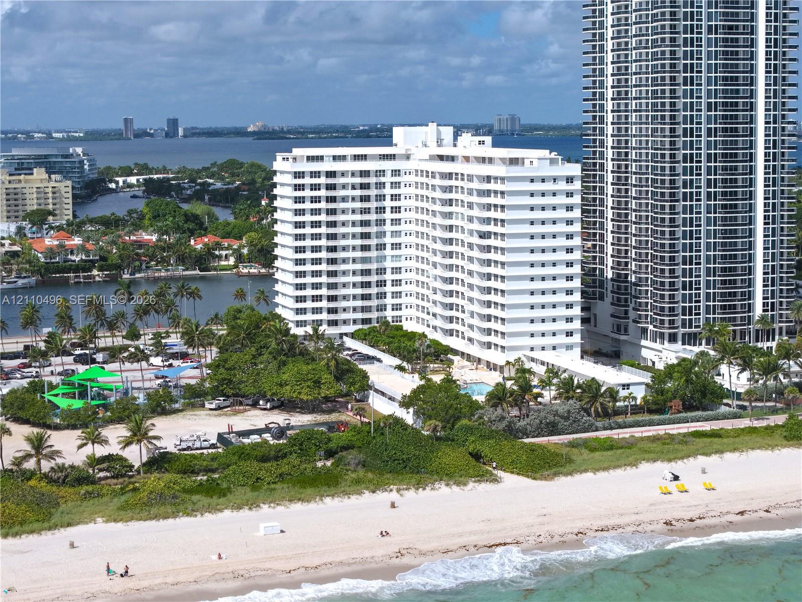 High-rise residential exterior situated on a sandy coastline featuring direct water access, an outdoor swimming pool, and tropical landscaping