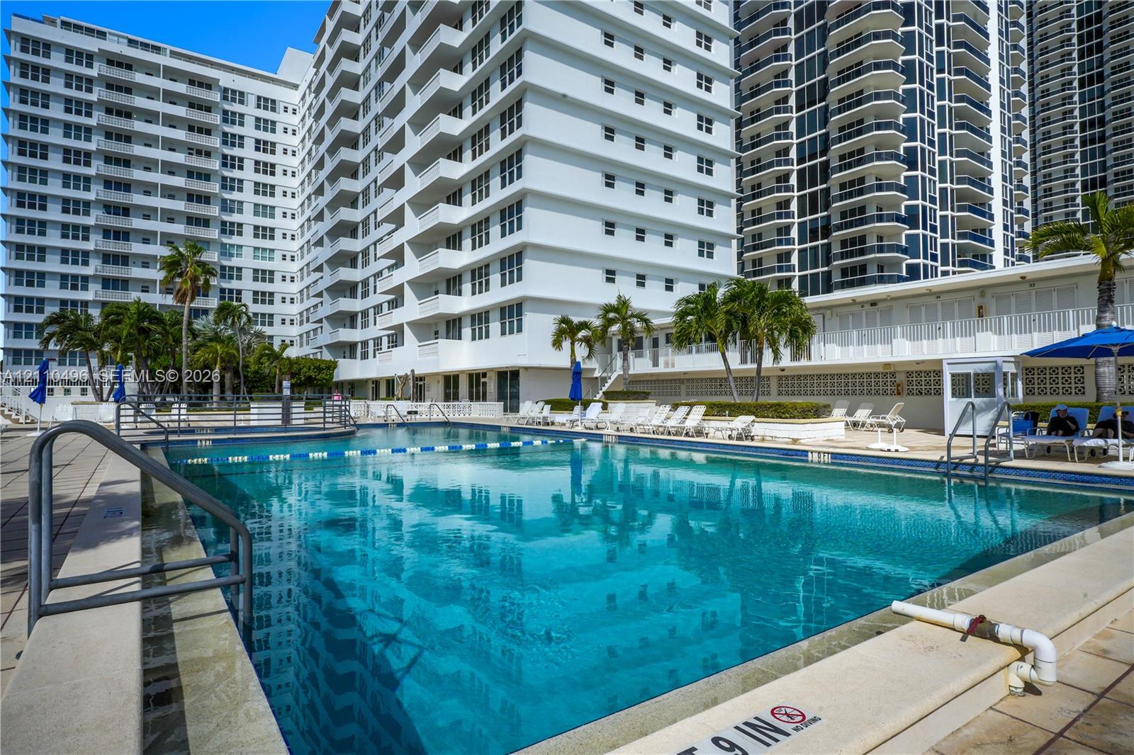 Large rectangular swimming pool with tile perimeter and metal handrails, situated on a stone-paved terrace