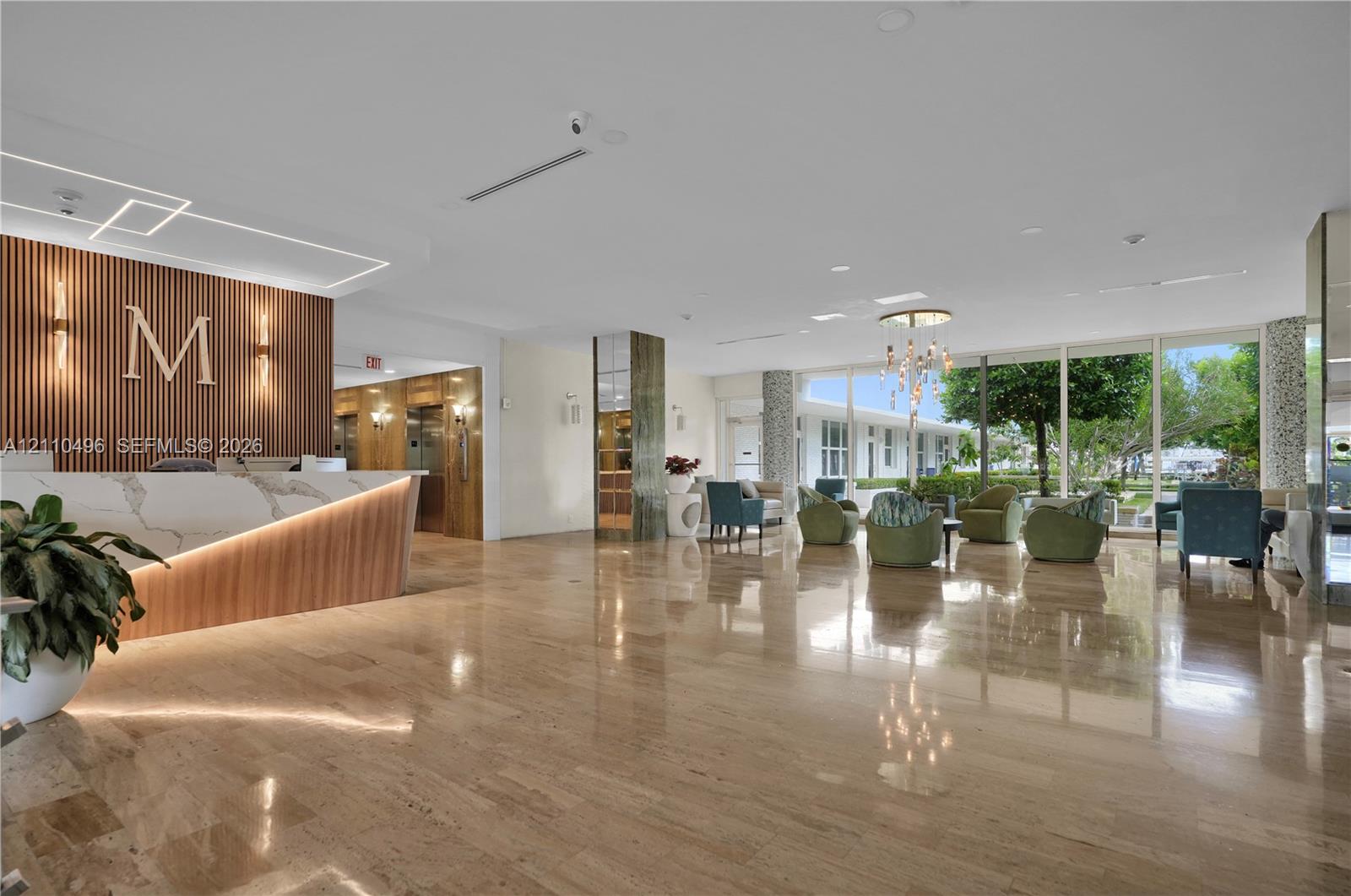 Lobby featuring polished stone flooring, custom reception desk with stone surfacing and wood-slat accent wall, floor-to-ceiling glass windows, and metallic feature lighting