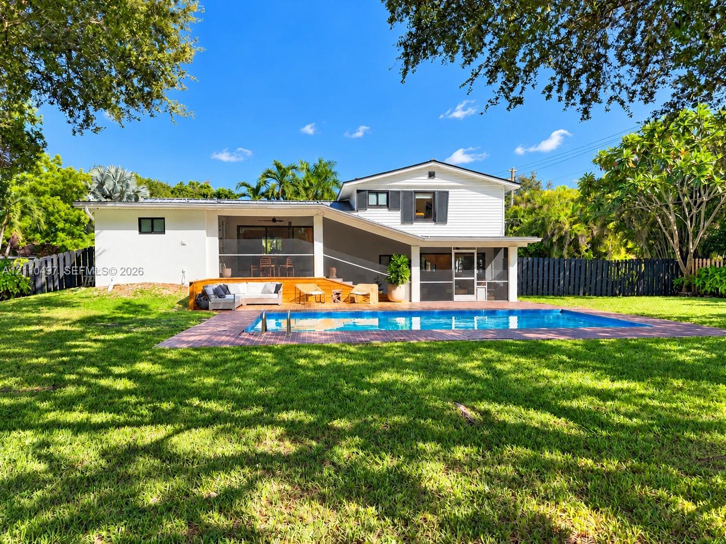 Rear exterior featuring an in-ground swimming pool, brick paver decking, a covered screened-in patio, and a fenced backyard