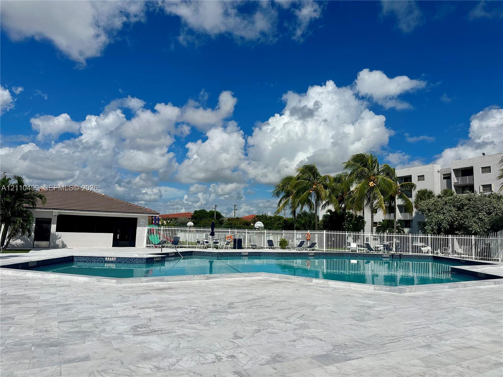 In-ground swimming pool with a tiled waterline and expansive stone paver deck, enclosed by perimeter fencing