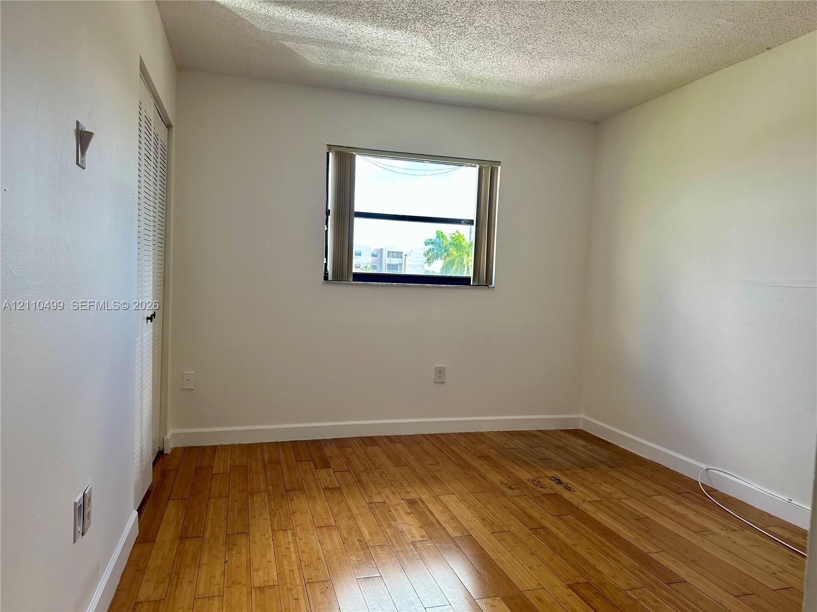 Room featuring wood-finish flooring, white walls, louvered closet doors, and a central window