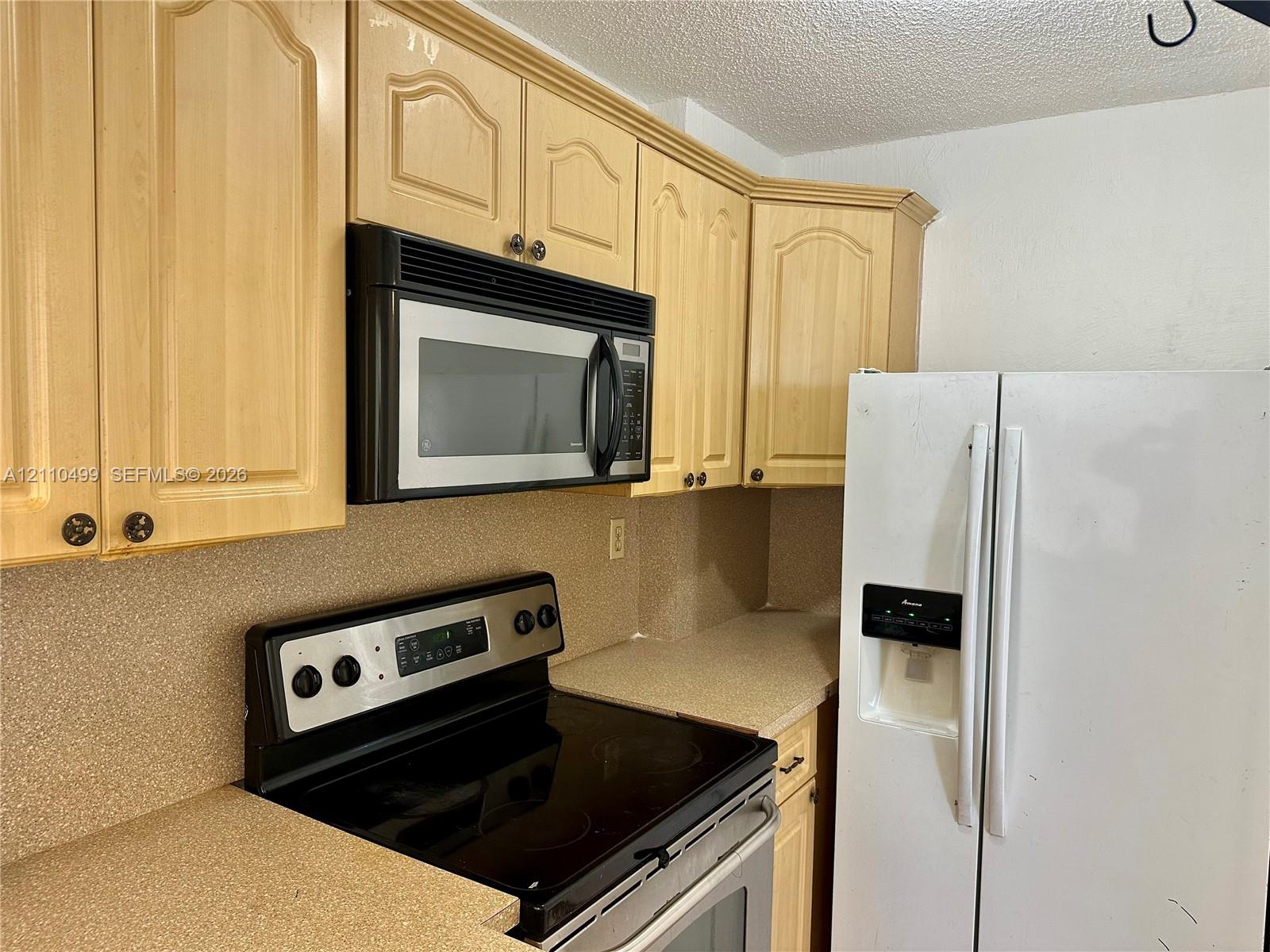 Kitchen featuring light-finish cabinetry, neutral-toned solid-surface countertops, integrated over-the-range microwave, electric range, and side-by-side refrigerator Kitchen featuring light-finish cabinetry, neutral-toned solid-surface countertops, integrated over-the-range microwave, electric range, and side-by-side refrigerator