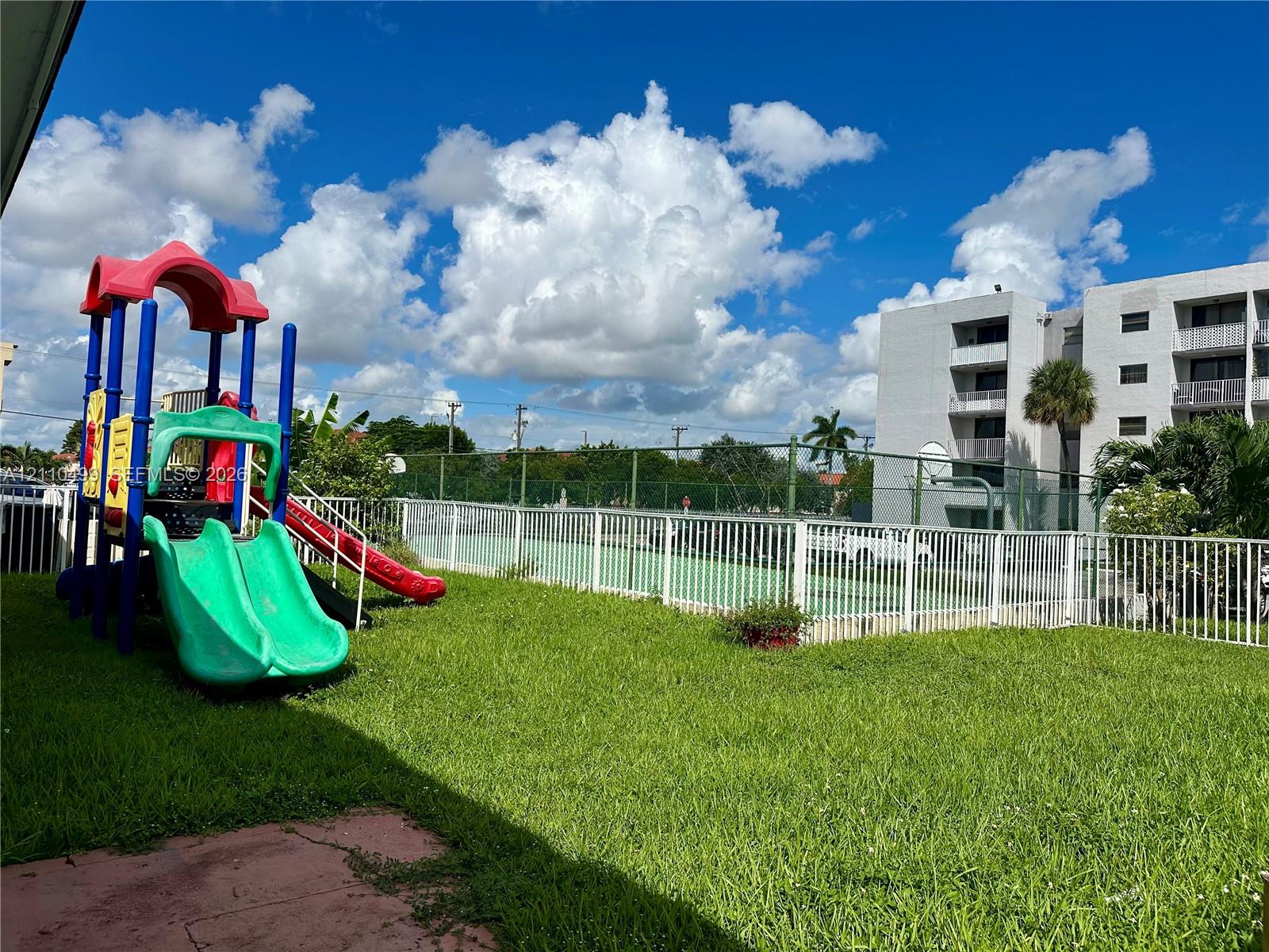 Common area featuring a grass lawn, fenced-in tennis court, and play equipment