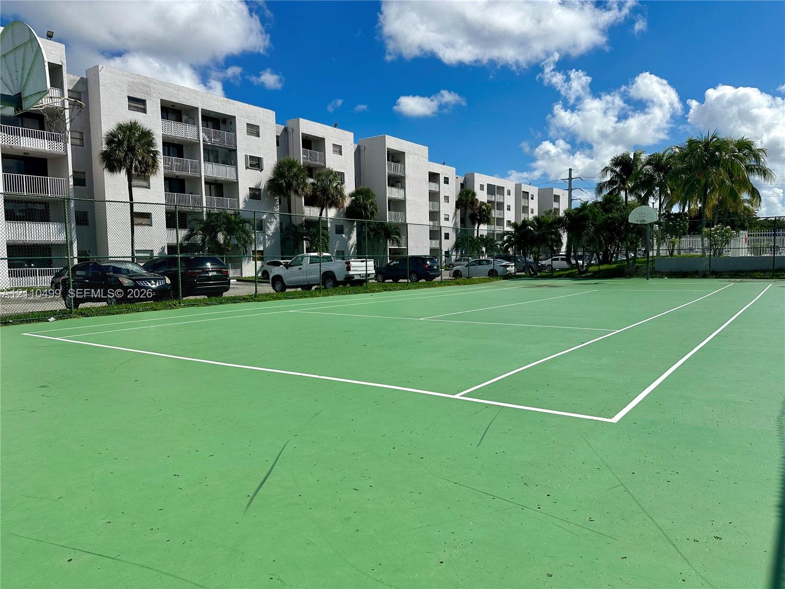 Tennis court featuring a hard surface, perimeter fencing, and an integrated basketball hoop