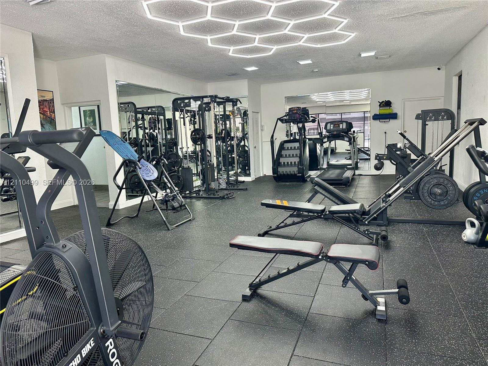 Fitness space featuring black rubberized flooring, large-scale wall-to-wall mirrors, and a custom hexagonal geometric LED ceiling light fixture