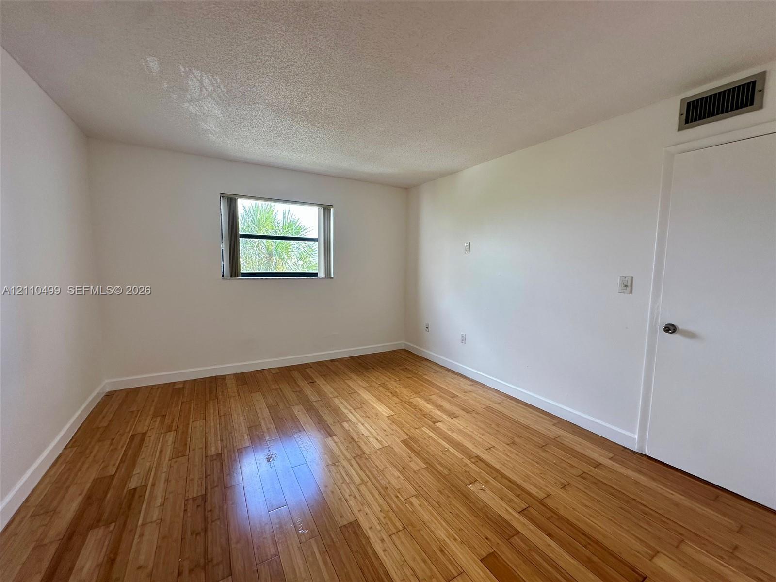 Room featuring wood-finish flooring, a single-pane window with a horizontal blind, and a solid-core interior door