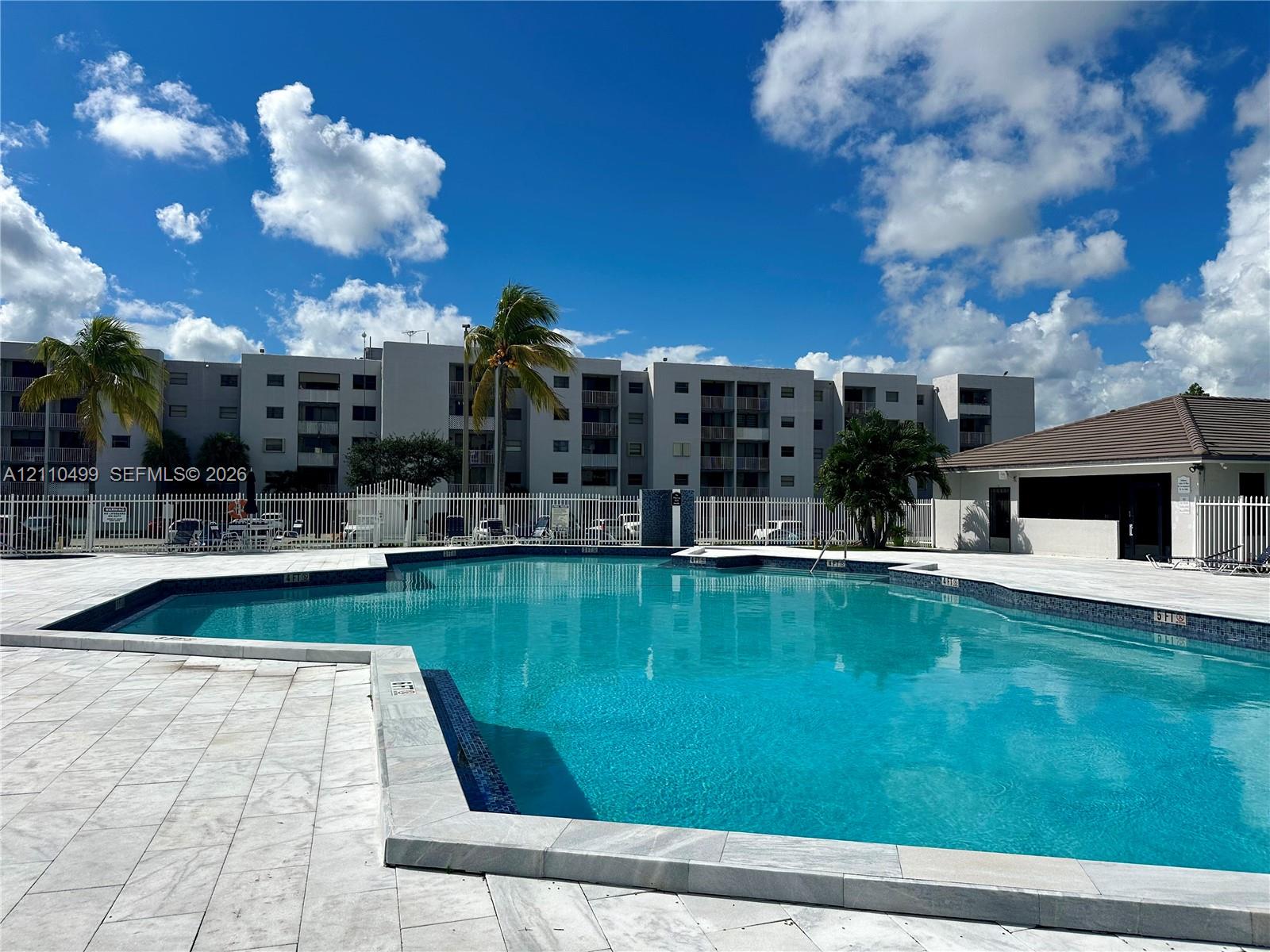 Swimming pool with tiled decking, perimeter fencing, and surrounding palm trees