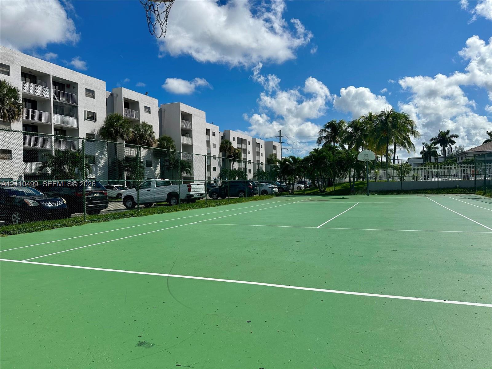 Outdoor recreation area featuring a paved multi-purpose court, chain-link perimeter fencing, and basketball goal
