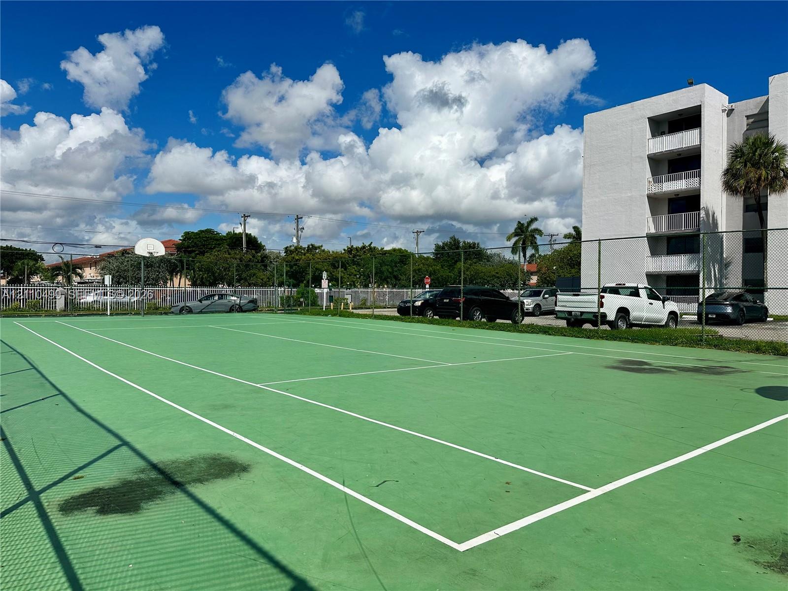 Recreational court featuring a fenced perimeter, hard-surface playing area, and integrated basketball hoop