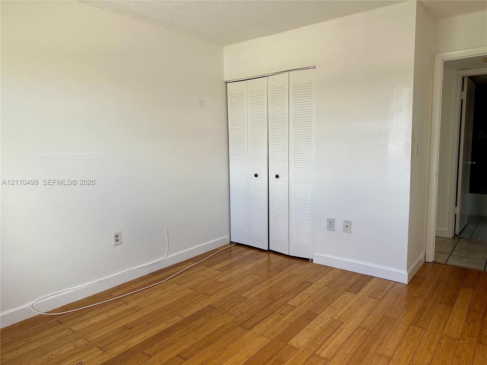 Room featuring wood-finish flooring, white walls, and a closet with white louvered bifold doors