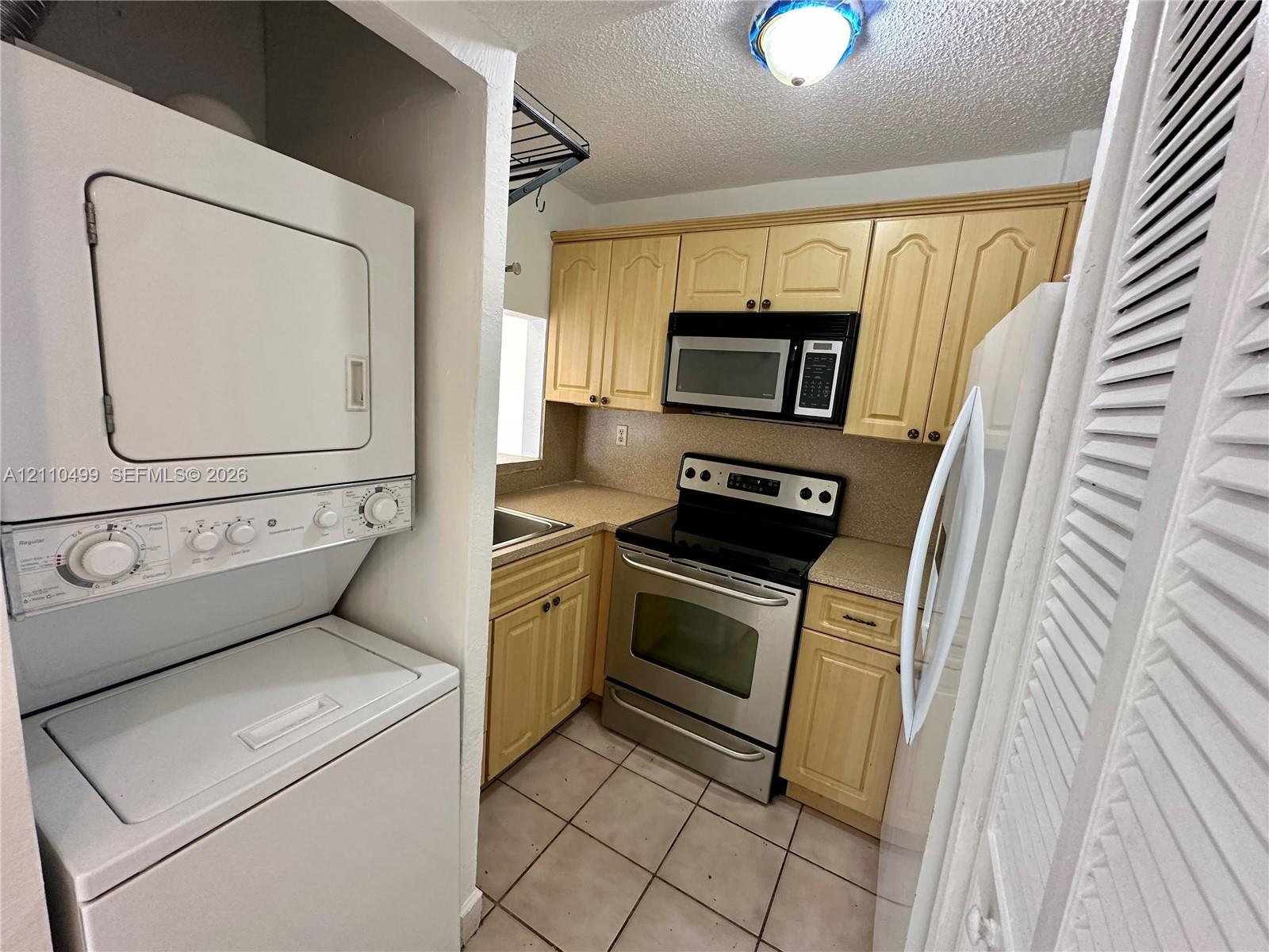 Kitchen featuring wood cabinetry, stainless steel appliances, a built-in microwave, tiled flooring, and an integrated laundry closet Kitchen featuring wood cabinetry, stainless steel appliances, a built-in microwave, tiled flooring, and an integrated laundry closet