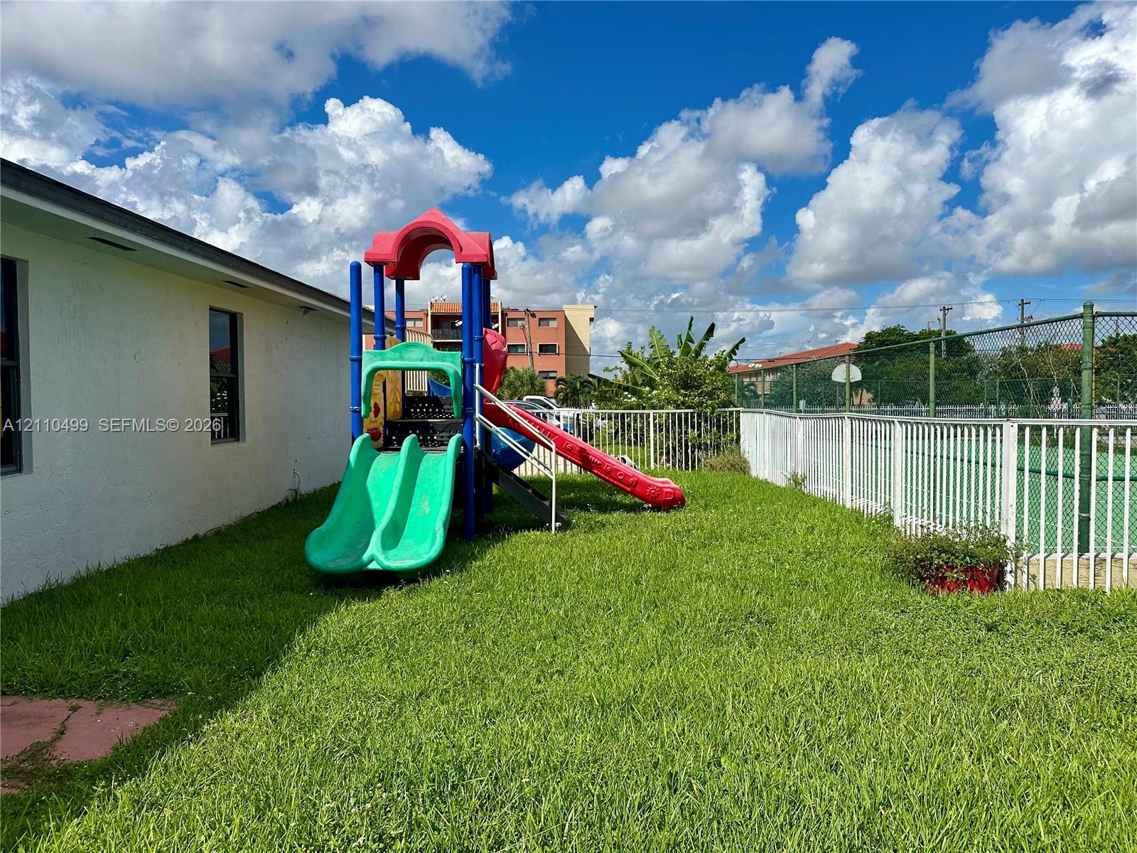 Outdoor space featuring a grass lawn, metal perimeter fencing, and a hard-surfaced sport court