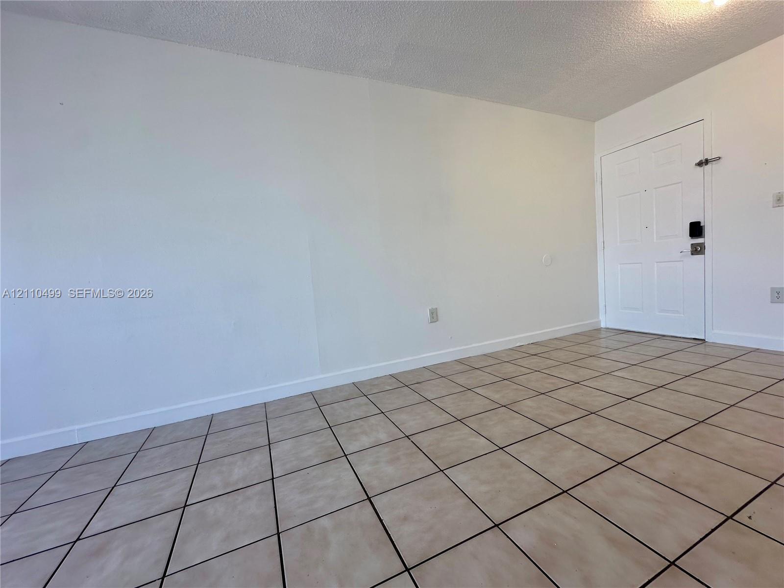 Neutral-toned interior space featuring white walls, square ceramic floor tile, and a white six-panel entry door with a digital deadbolt Neutral-toned interior space featuring white walls, square ceramic floor tile, and a white six-panel entry door with a digital deadbolt