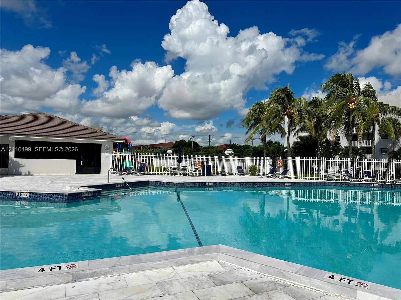 Swimming pool with stone-finish decking, tiled waterline, and white metal perimeter fencing