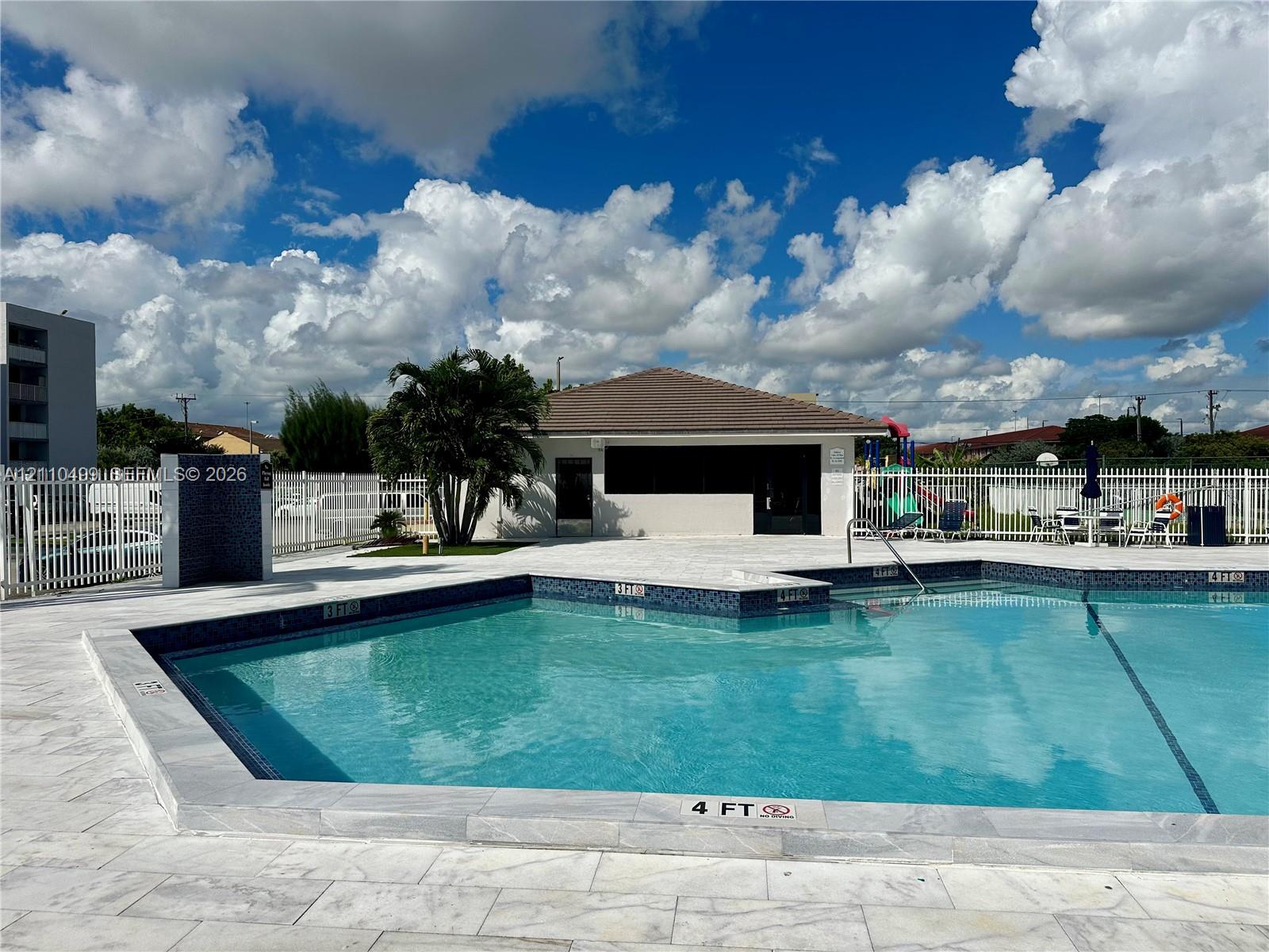 Swimming pool with stone-tiled decking, decorative tile waterline, and surrounding metal fencing