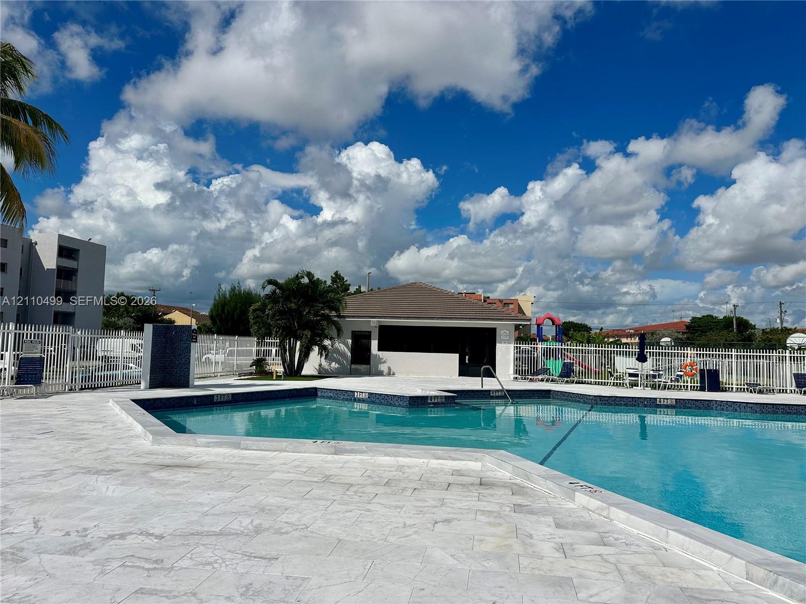 In-ground swimming pool with tile trim, expansive stone-paver pool deck, and enclosed perimeter fencing