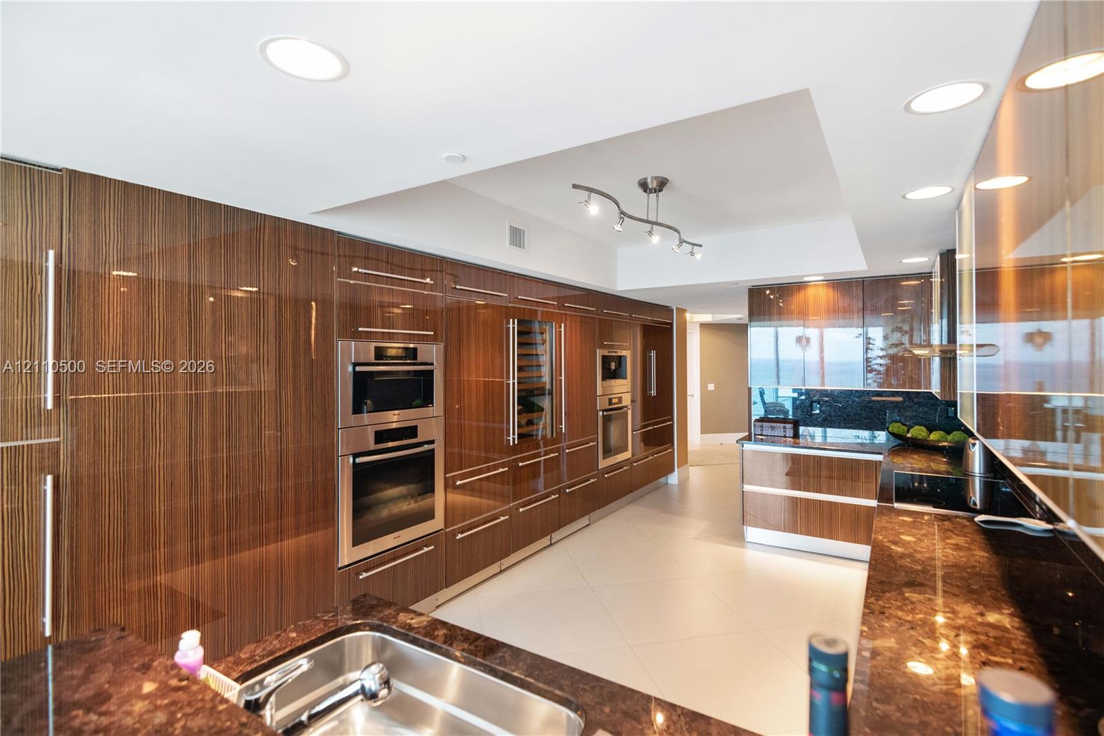 Modern kitchen featuring high-gloss wood-finish cabinetry, stone countertops, stainless steel wall ovens, a built-in wine cooler, and recessed lighting