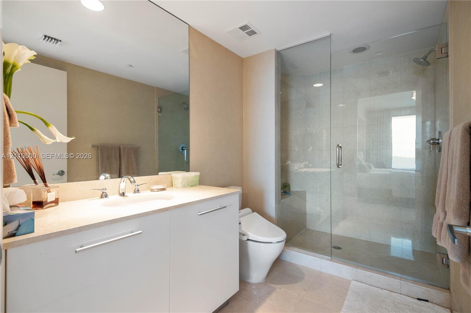 White cabinetry vanity with a solid surface countertop, an expansive wall-mounted mirror, and a glass-enclosed walk-in shower with tile surround