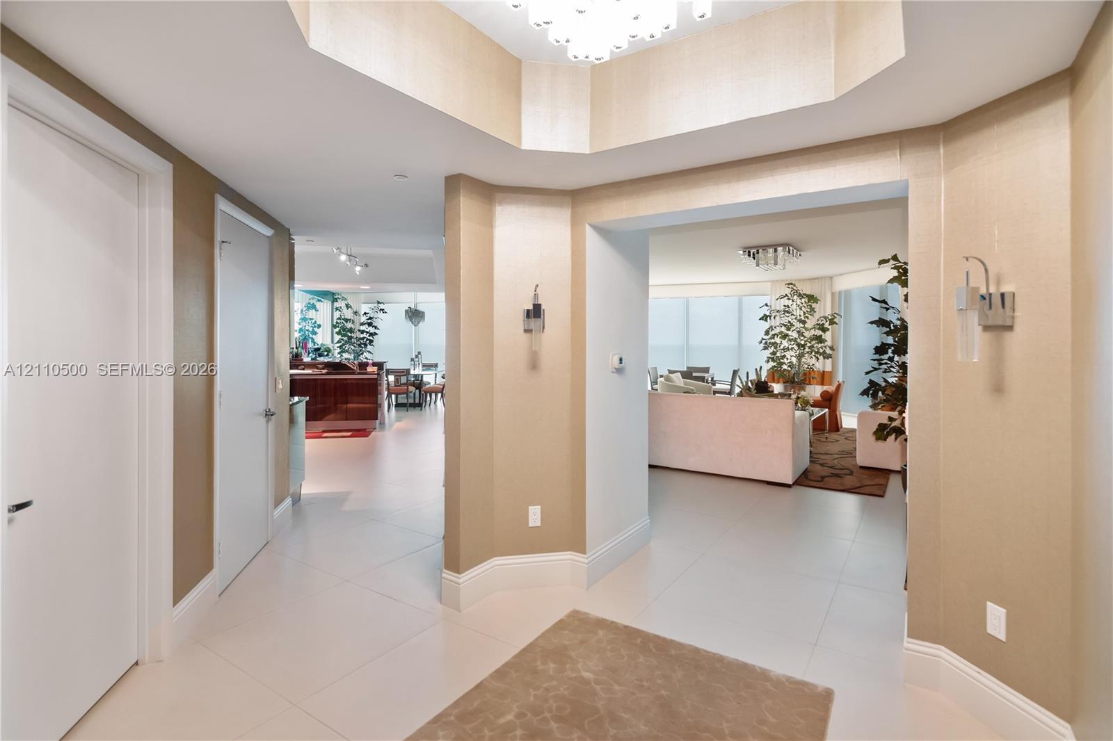 Foyer featuring a recessed tray ceiling, large-format tile flooring, textured wall finishes, and wall-mounted metal sconces