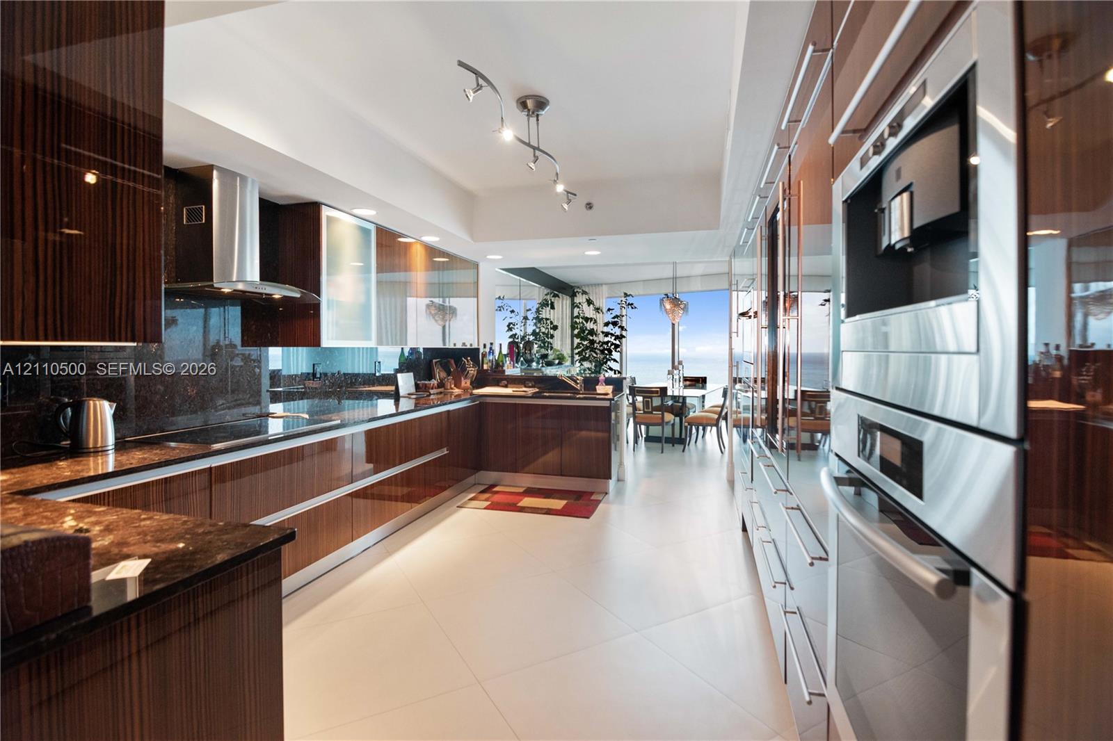 High-gloss cabinetry, stone countertops, built-in stainless steel double wall ovens, stainless steel range hood, and tile flooring