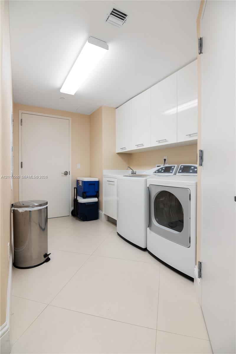 Laundry area featuring large-format tile flooring, white cabinetry, integrated countertop with sink, and recessed ceiling lighting