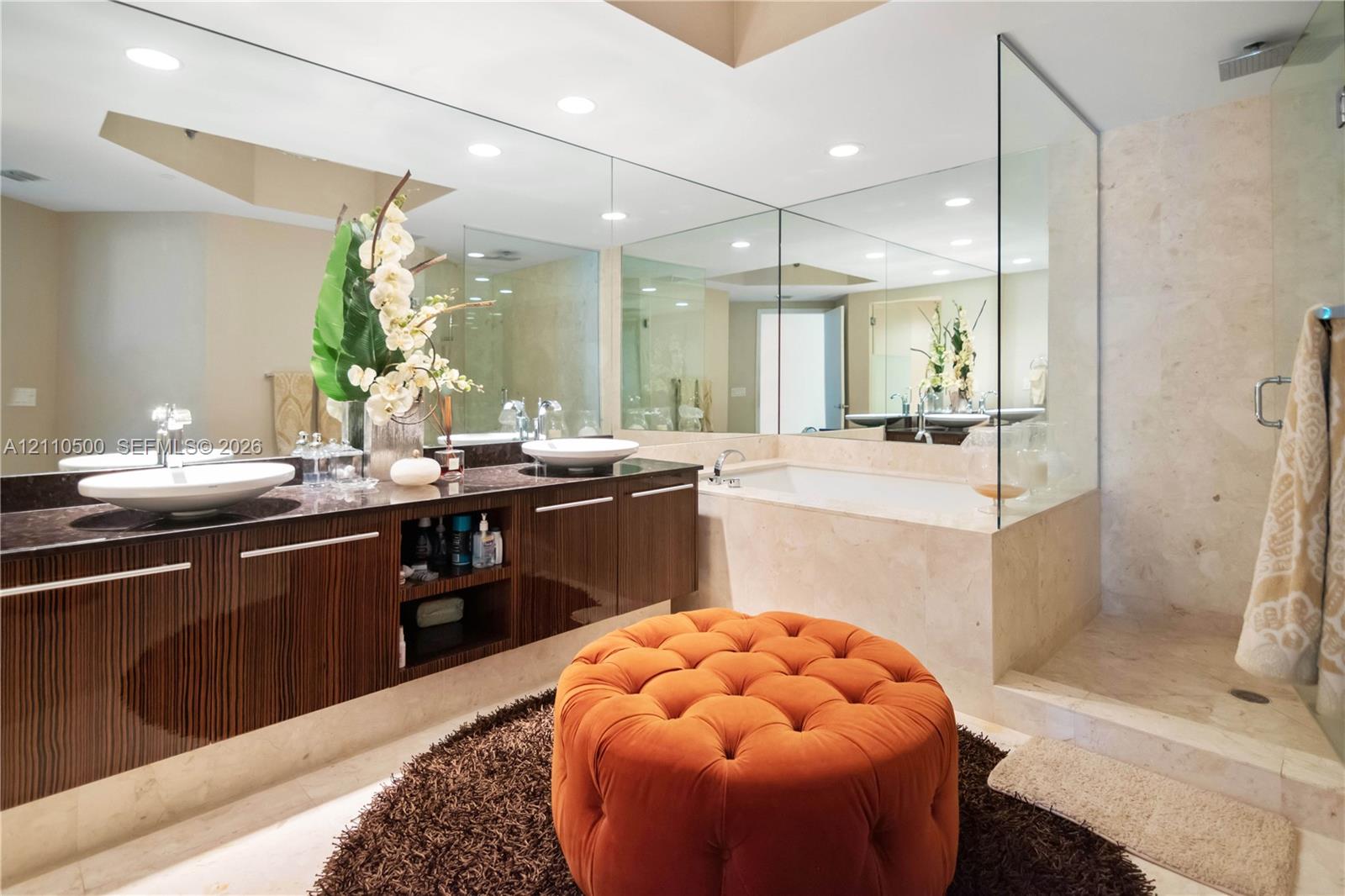 Floating vanity with dual vessel sinks and stone countertop, recessed lighting, expansive wall-to-wall mirror, built-in soaking tub with stone surround, and glass-enclosed walk-in shower