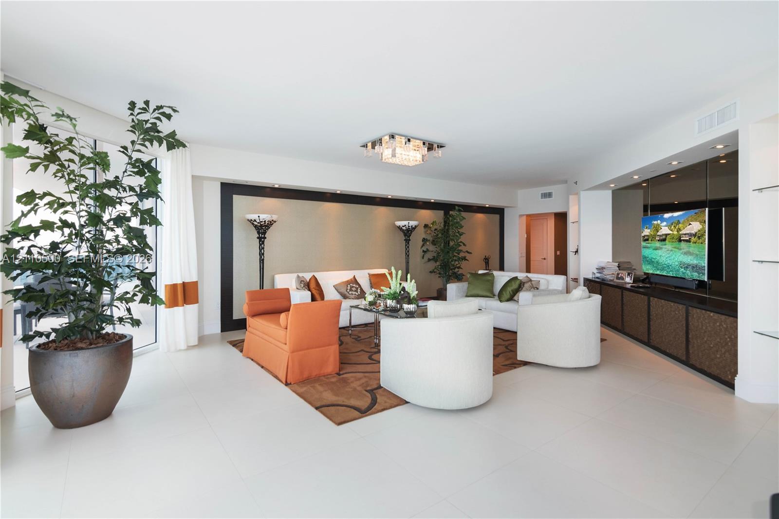 Living area featuring oversized floor-to-ceiling windows, large-format tile flooring, built-in entertainment cabinetry with integrated recessed lighting, and a tiered crystalline flush-mount ceiling fixture