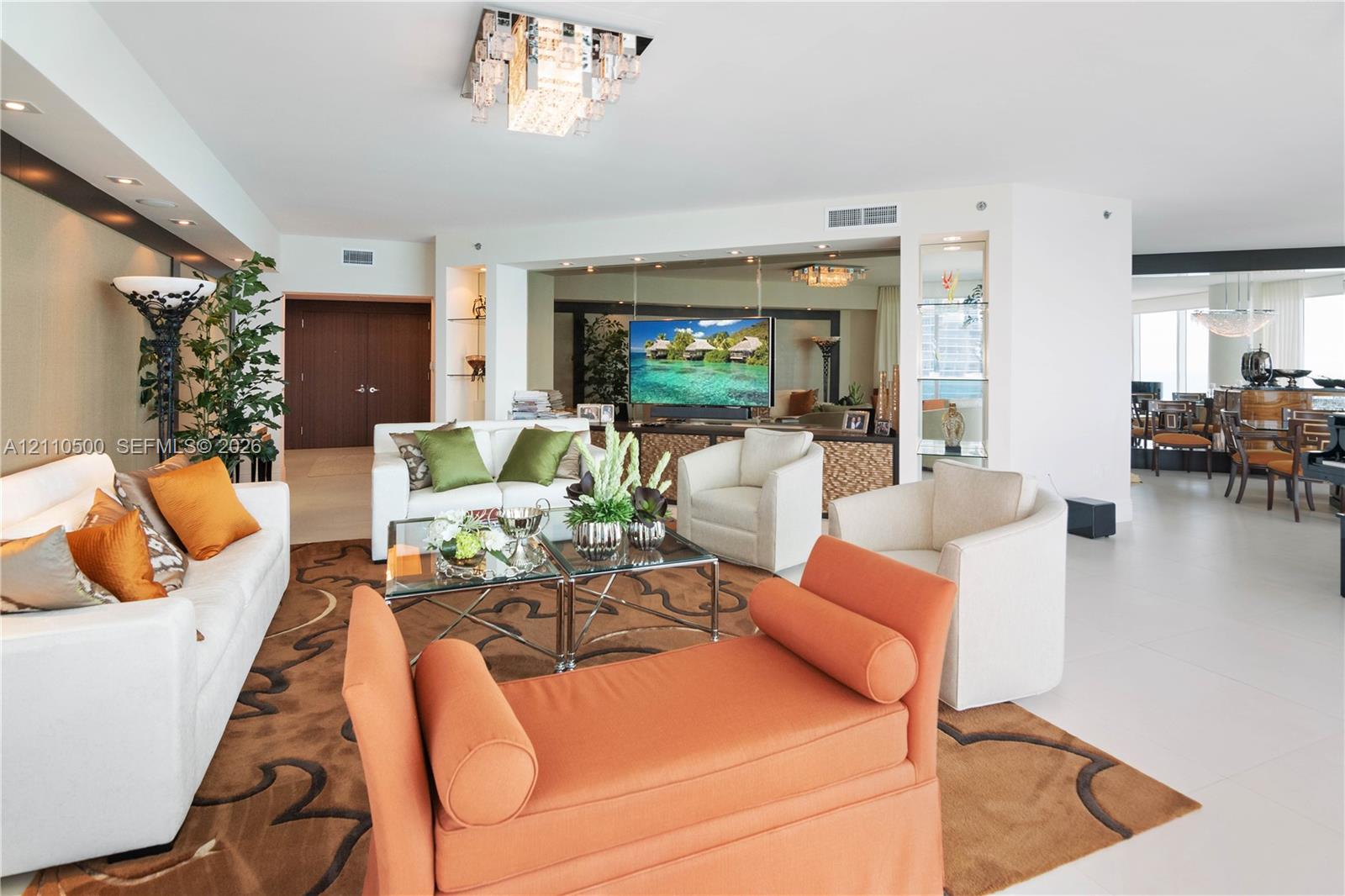 Open-concept living space featuring large-format tile flooring, built-in recessed wall shelving, mirrored accent walls, and a multi-tiered crystal flush-mount light fixture