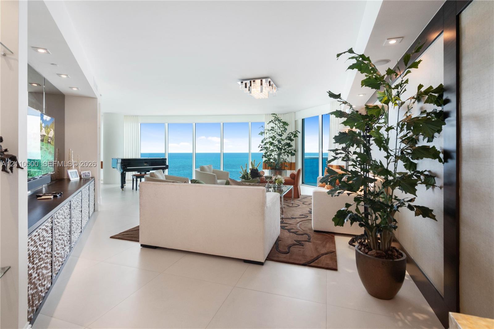Floor-to-ceiling windows, large-format tile flooring, recessed ceiling lighting, built-in cabinetry with textured paneling, and a geometric chandelier